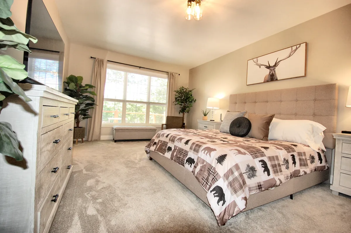 A tranquil bedroom featuring a bed with patterned bedding, a large window that lets in abundant natural light, and stylish decorative wall art with an antler motif. The cozy space is designed for relaxation, with plush bedding that looks inviting and comfortable.