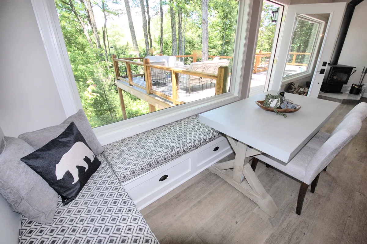 A cozy seating area inside, with a dining table positioned next to a large window that offers views of the surrounding greenery. The setup is ideal for enjoying meals, working with serene views, or simply relaxing and watching nature outside.