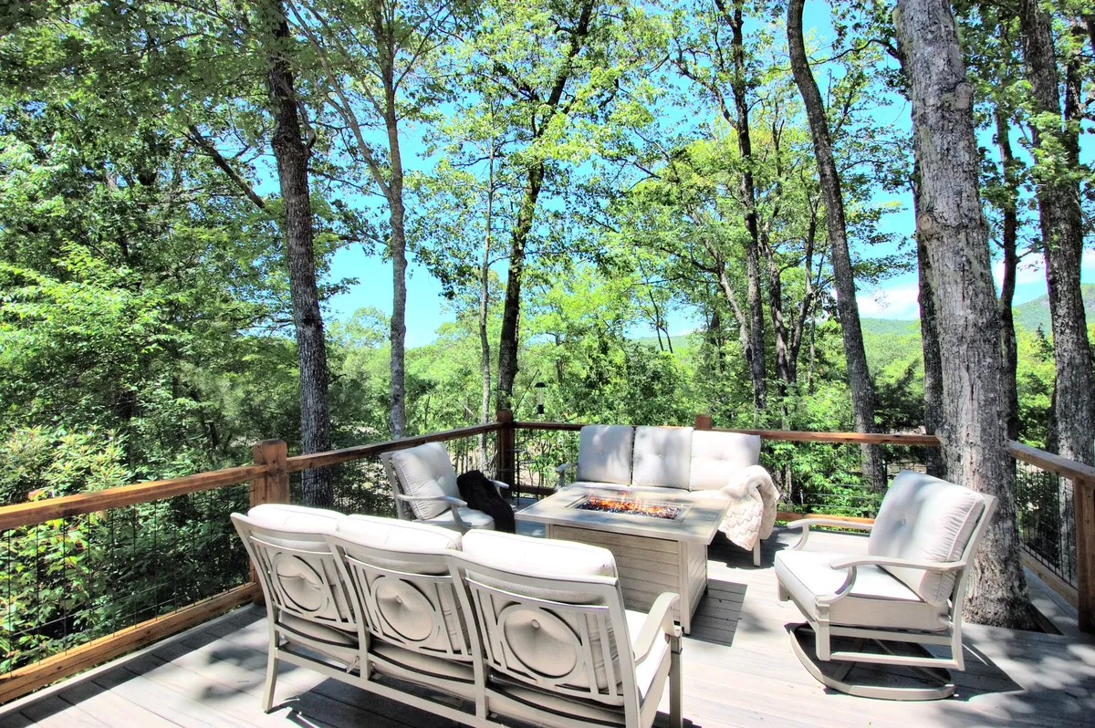 A comfortable outdoor seating arrangement centered around a fire pit on the deck, with surrounding trees creating a serene, private ambiance. The setup is perfect for enjoying warm conversations and cozy evenings under the stars.