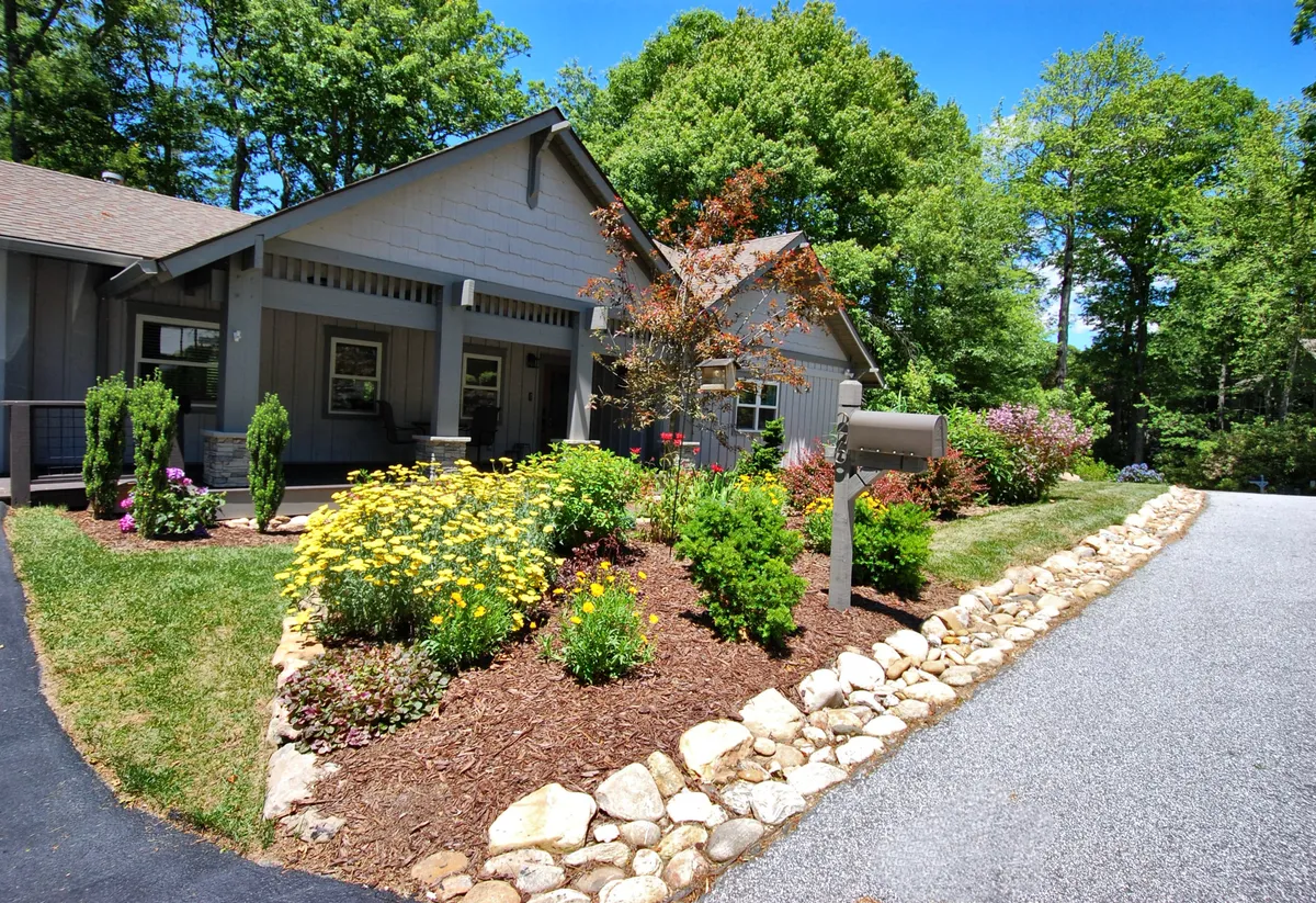 A welcoming exterior view of Jessamine Cottage, showing vibrant flower beds, a well-maintained lawn, and a stone pathway leading to a cozy front porch. The space feels lively and ready for social gatherings or family moments.