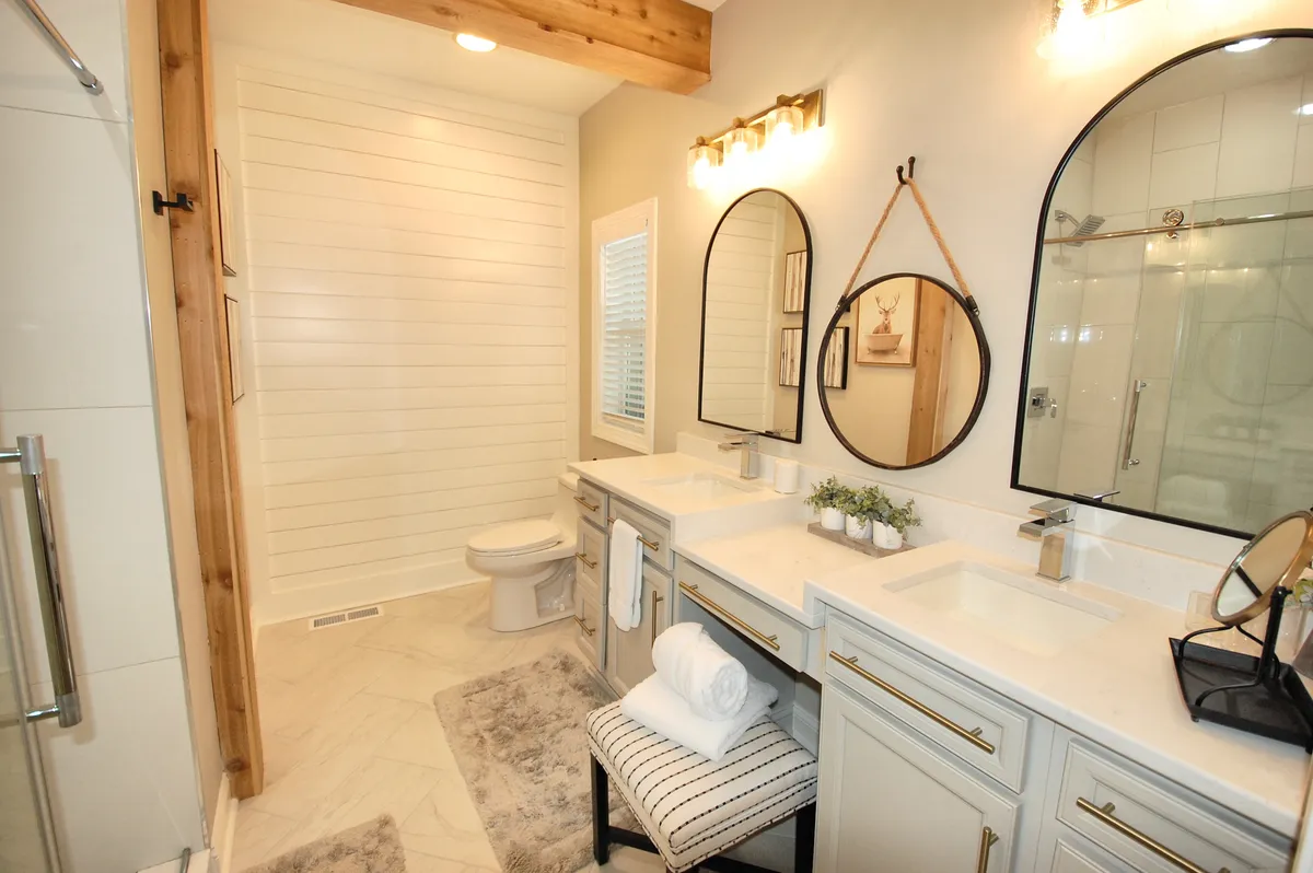 A modern, serene bathroom featuring double sinks with mirrors, natural wood accents, contemporary light fixtures, and a glimpse of a spacious shower area. The space feels clean, refreshing, and designed for comfort and convenience.