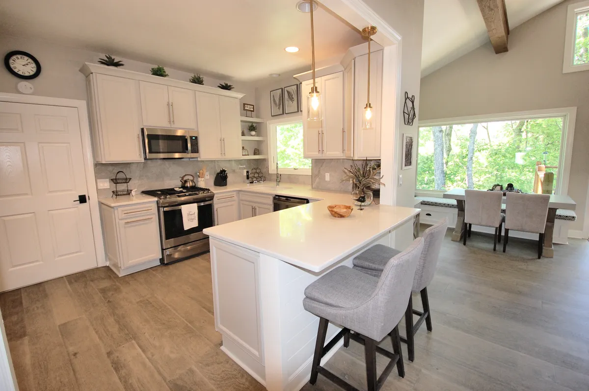 This image captures a modern kitchen with sleek cabinetry, a central island with seating, and large windows that bathe the space in natural light. The layout encourages both meal preparation and casual dining, while the view of nature outside adds a refreshing atmosphere.